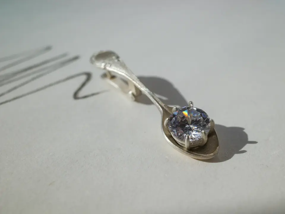 A silver spoon holding a small stone, on white paper
