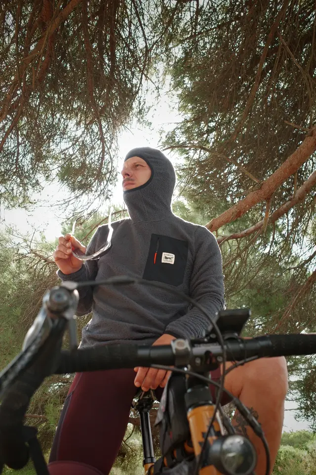 A cyclist in a balaclava riding through pine trees