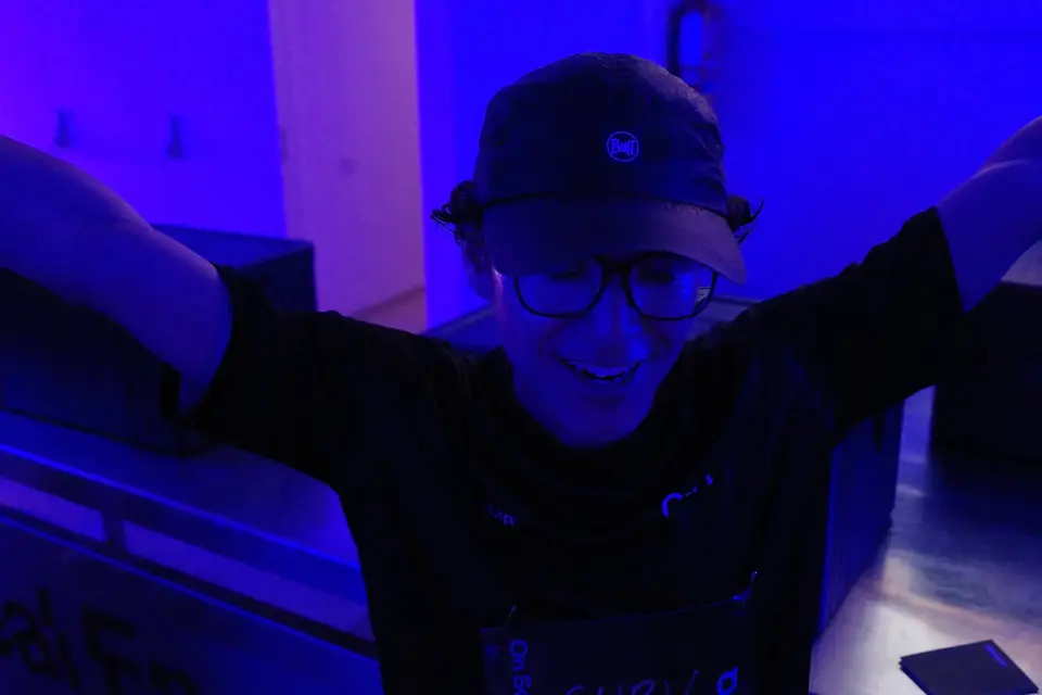 A person with arms raised, smiling in blue light